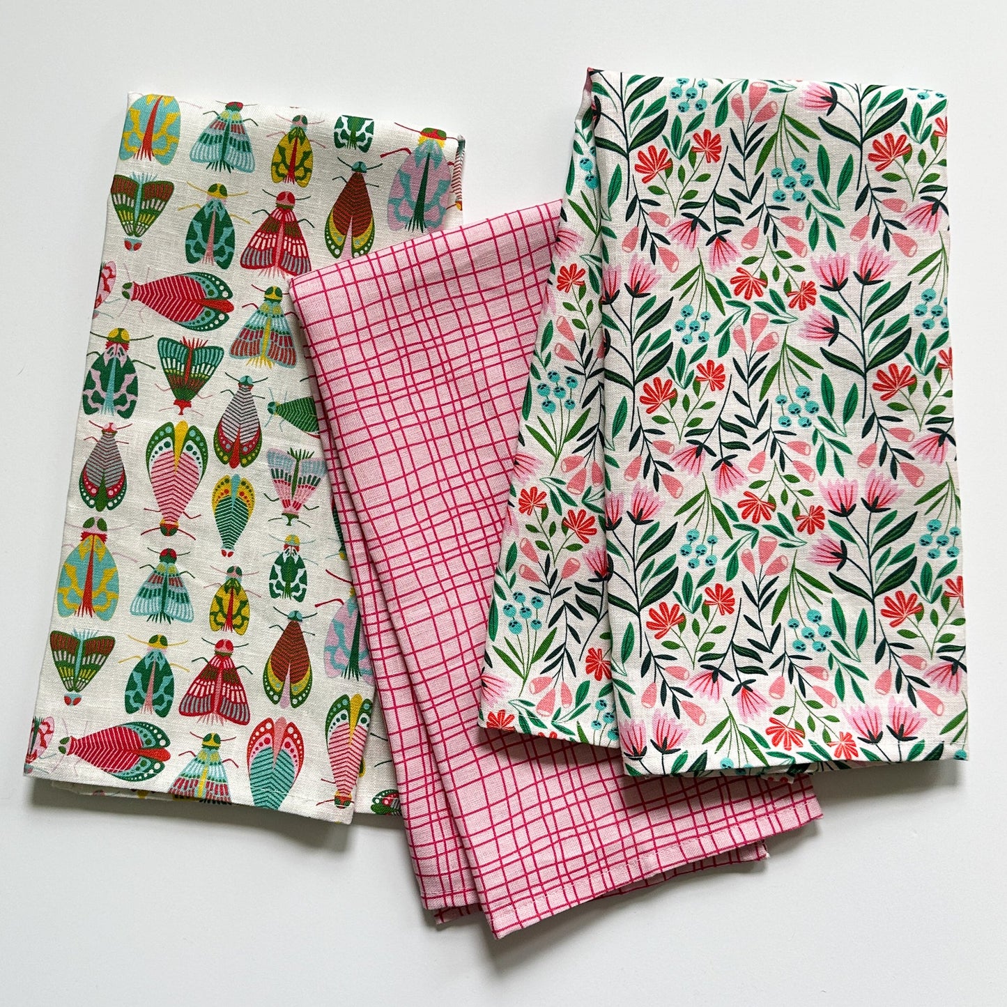 Three bright tea towels with different patterns on a white background drawn by Rebecca Woolbright.