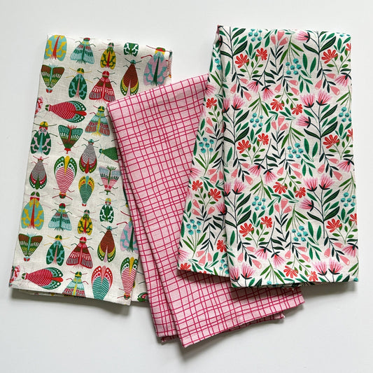 Three colorful patterned tea towels displayed together as a flat lay. All patterns drawn by Rebecca Woolbright.