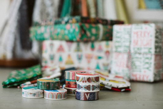 A table filled with colorful, patterned presents, washi tape and folded tea towels all designed by Rebecca Woolbright.
