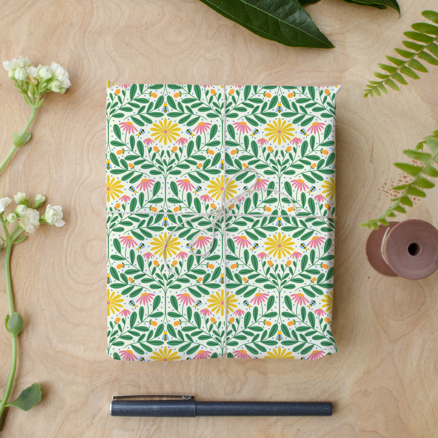 Floral gift wrap sheets with bees and bright blooms tied with twine on wood desk, Bee Kind wrapping paper