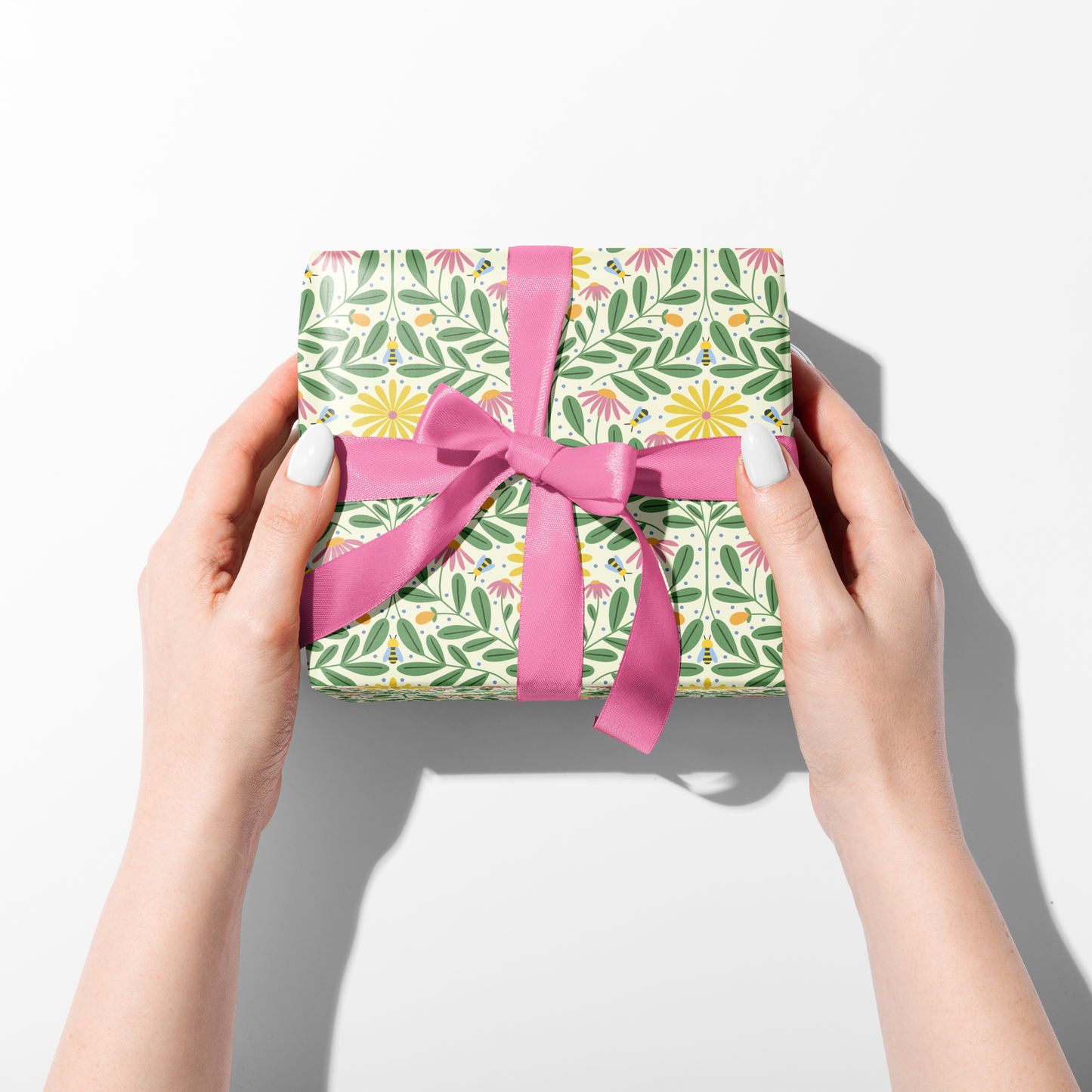 Hands holding wrapped gift in Bee Kind floral gift wrap with pink ribbon, cheerful spring wrapping paper