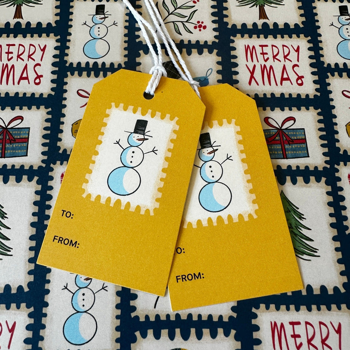Cute snowmen on a gift tag set against postage stamp wrapping paper