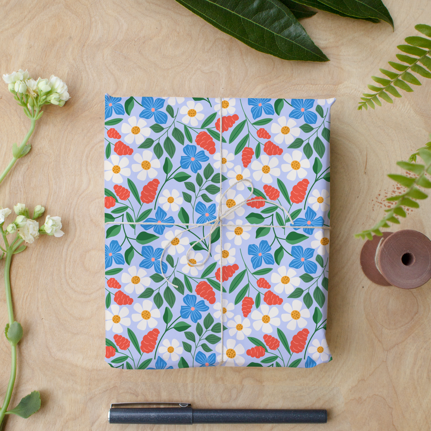 Floral wrapping paper sheets with daisies and blue flowers tied with twine on wood desk, Garden Path gift wrap