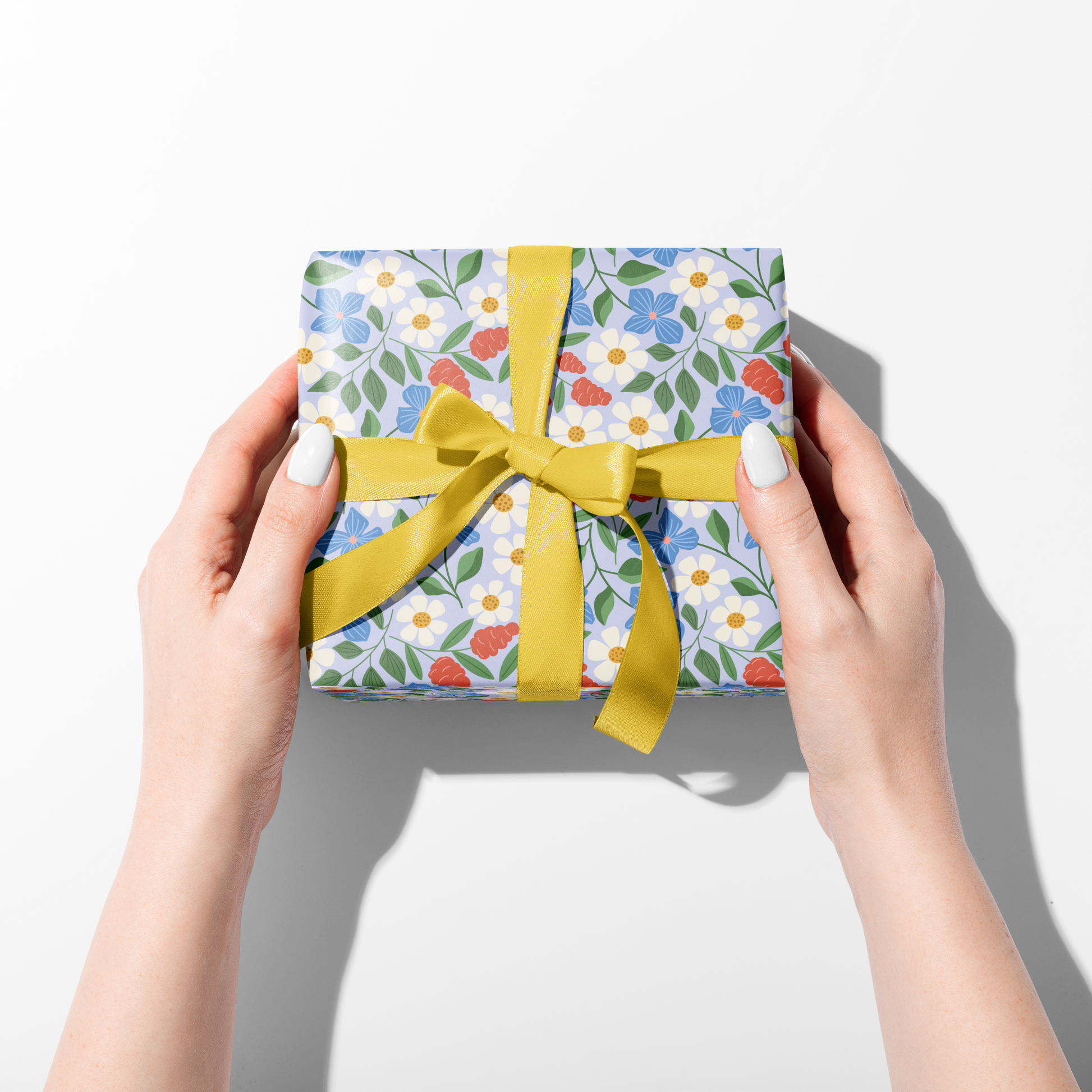 Hands holding wrapped gift in Garden Path floral wrapping paper with yellow ribbon, cheerful spring gift wrap