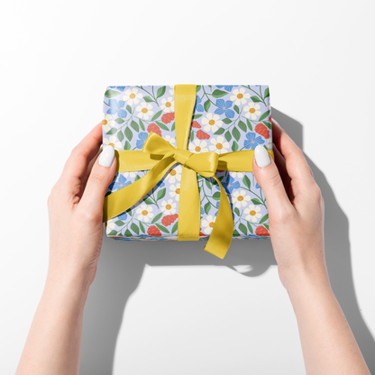 Hands holding wrapped gift in Garden Path floral wrapping paper with yellow ribbon, cheerful spring gift wrap