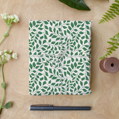 Green leafy wrapping paper sheets tied with twine on wood desk, botanical gift wrap flat lay