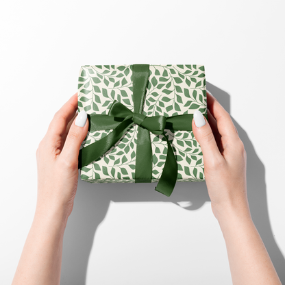 Hands holding wrapped gift in green botanical wrapping paper with dark green ribbon, eco friendly gift wrap