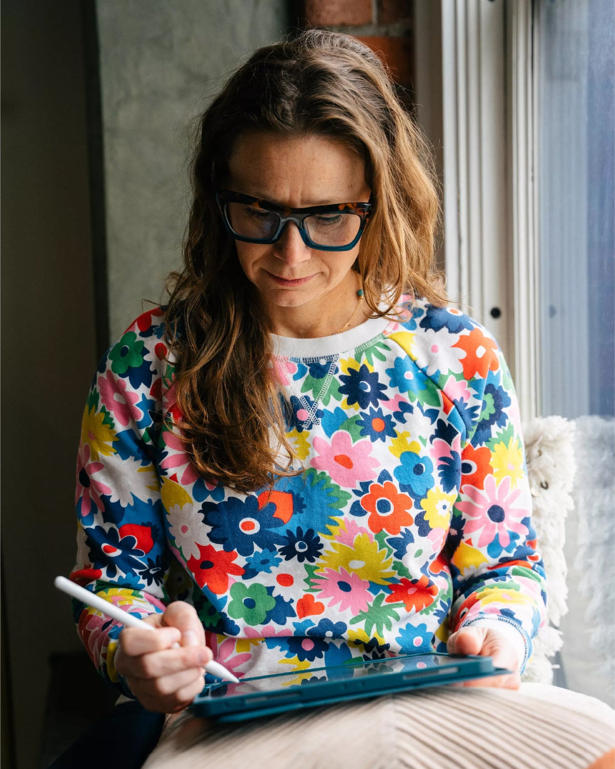 A woman in a colorful sweatshirt working on an ipad
