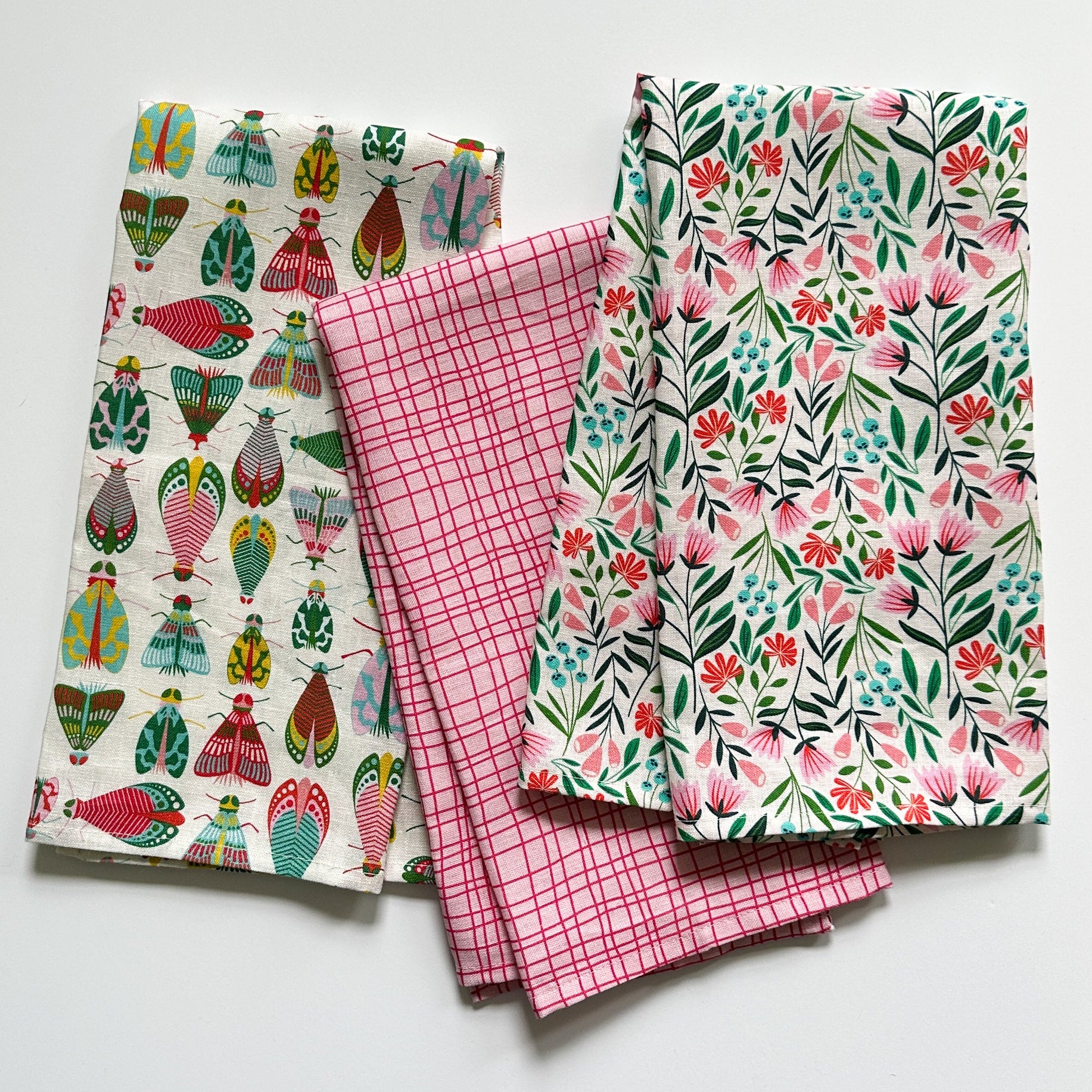 Three bright tea towels with different patterns on a white background drawn by Rebecca Woolbright.