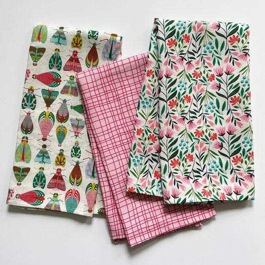Three bright tea towels with different patterns on a white background drawn by Rebecca Woolbright.