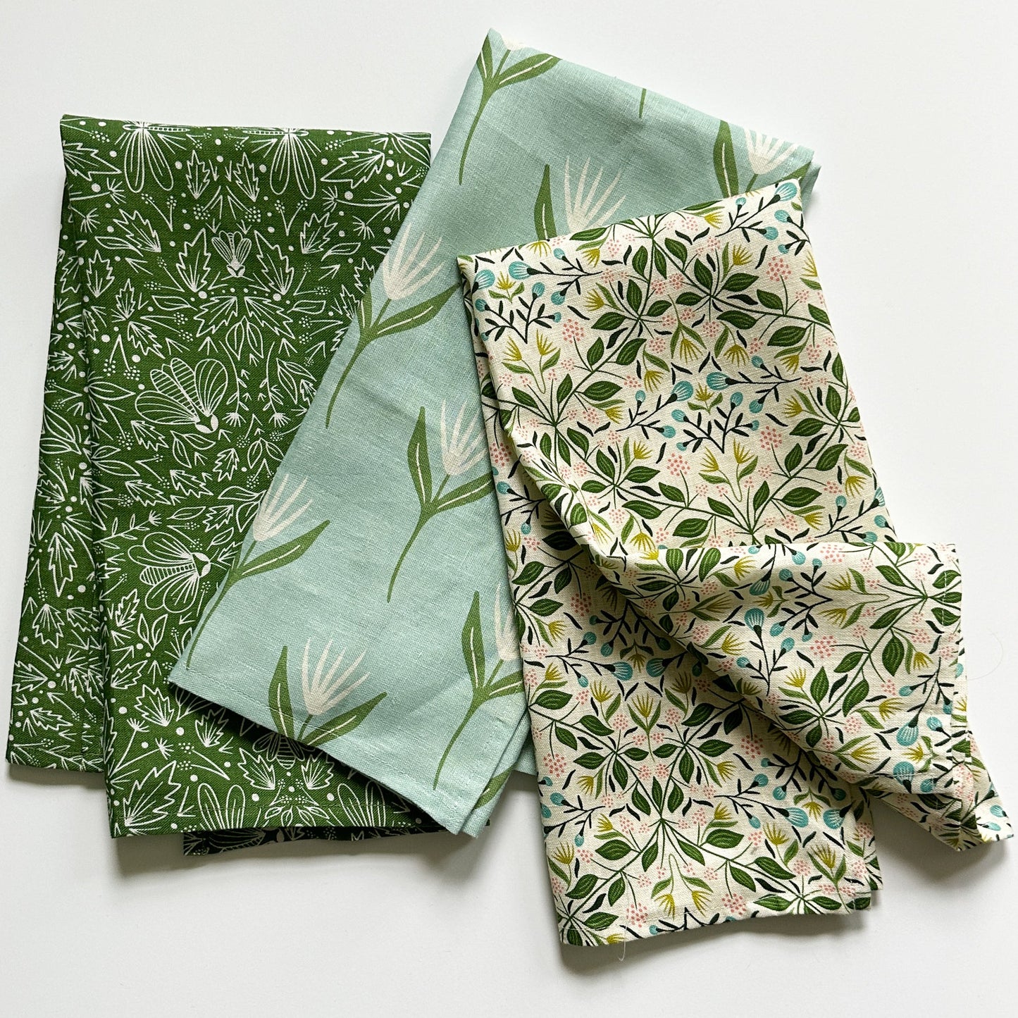 Three patterned tea towels with green and natural patterns on a white background