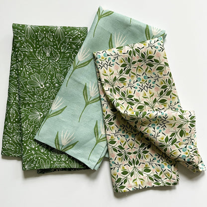 Three patterned tea towels with green and natural patterns on a white background