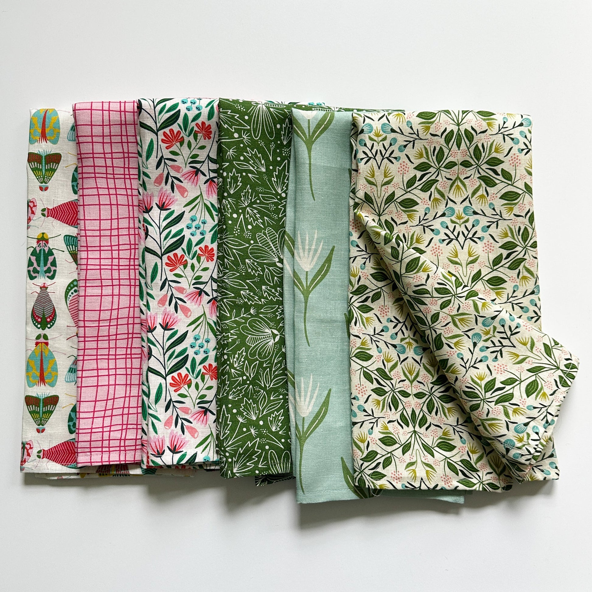 Six folded colorful tea towels with various patterns on a white background illustrated by Rebecca Woolbright