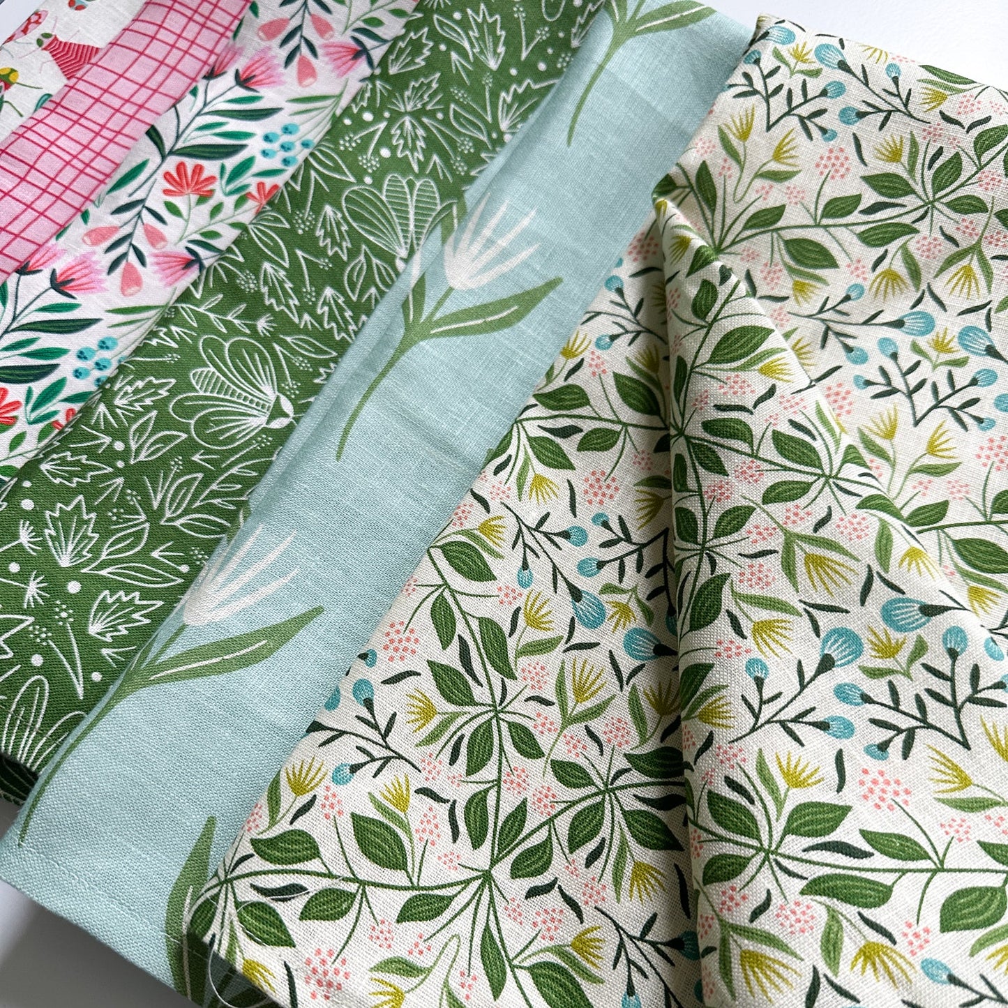 Collection of floral and leaf-patterned tea towels on a white background illustrated by Rebecca Woolbright.