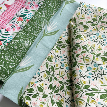 Collection of floral and leaf-patterned tea towels on a white background illustrated by Rebecca Woolbright.