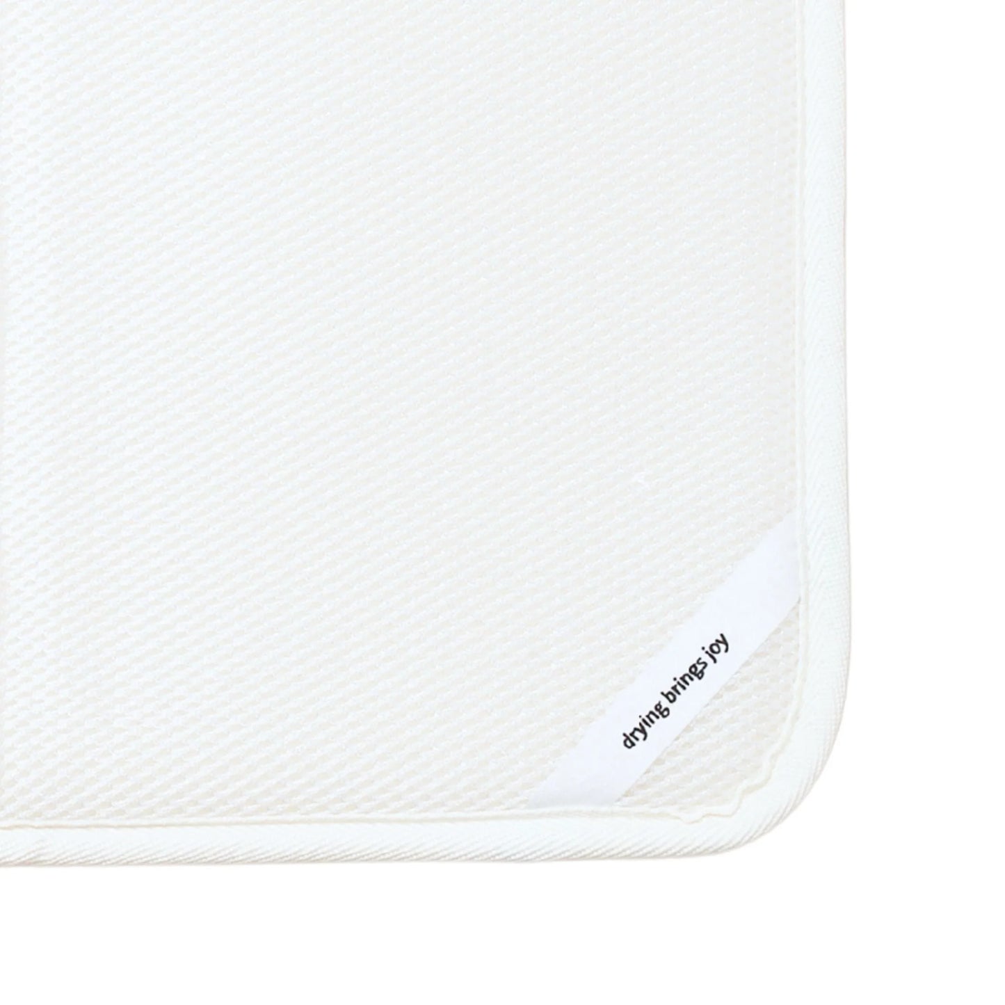 Close-up of a white textured dish mat with a white border and a small white corner tab printed with the brand name 'drying brings joy' in black text.