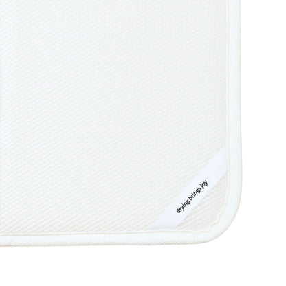 Close-up of a white textured dish mat with a white border and a small white corner tab printed with the brand name 'drying brings joy' in black text.